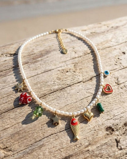 Delicate pearl charm beaded necklace with enamel charms resting on textured wooden surface, showcasing seaside-inspired jewelry with natural lighting.