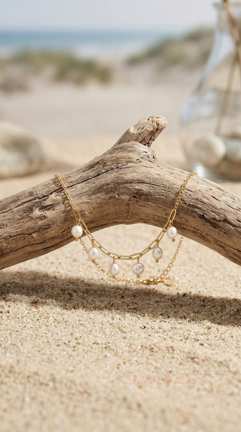 Close-up of a delicate gold anklet with dangling pearls resting on driftwood outdoors, highlighting its fine craftsmanship.