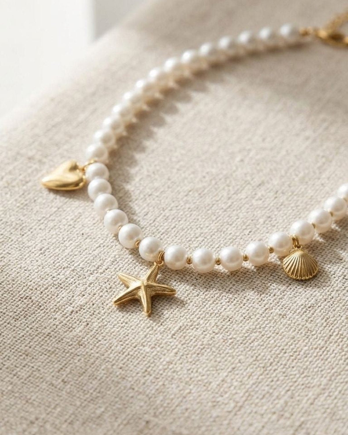 Close-up of the 'Pearl Sea Day' necklace with imitation pearls and sea-themed charms on textured fabric, showcasing its delicate shimmer and coastal style.