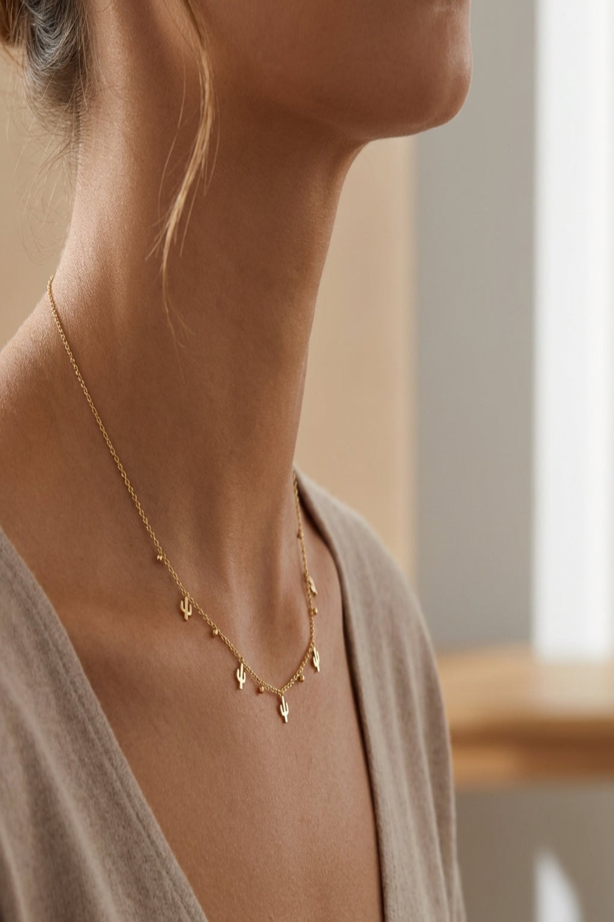 Petite stainless steel cactus charm necklace draped around a female model's neck, highlighting fine chain and detailed cactus pendants in a minimalist studio setting.