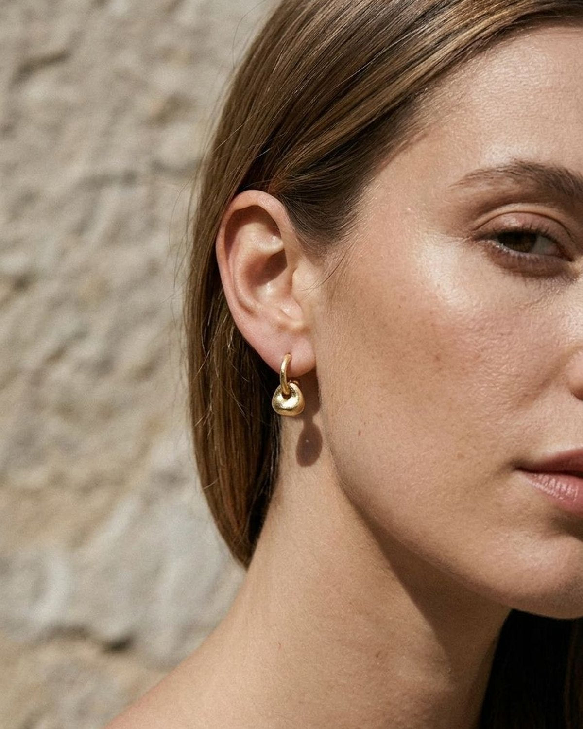 Petite irregular gold drop earrings worn on earlobes for a simple and chic everyday jewelry look.