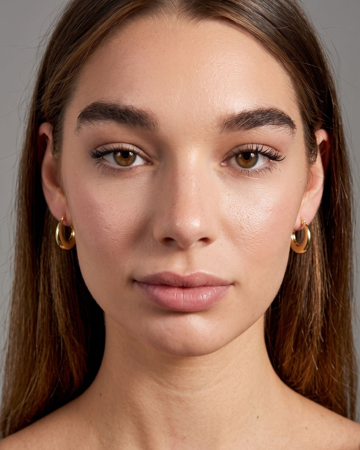 Close-up front view of small stainless steel hoop earrings worn on earlobes with distinct highlights from directional light.