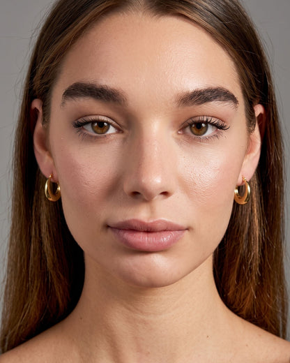 Close-up front view of small stainless steel hoop earrings worn on earlobes with distinct highlights from directional light.