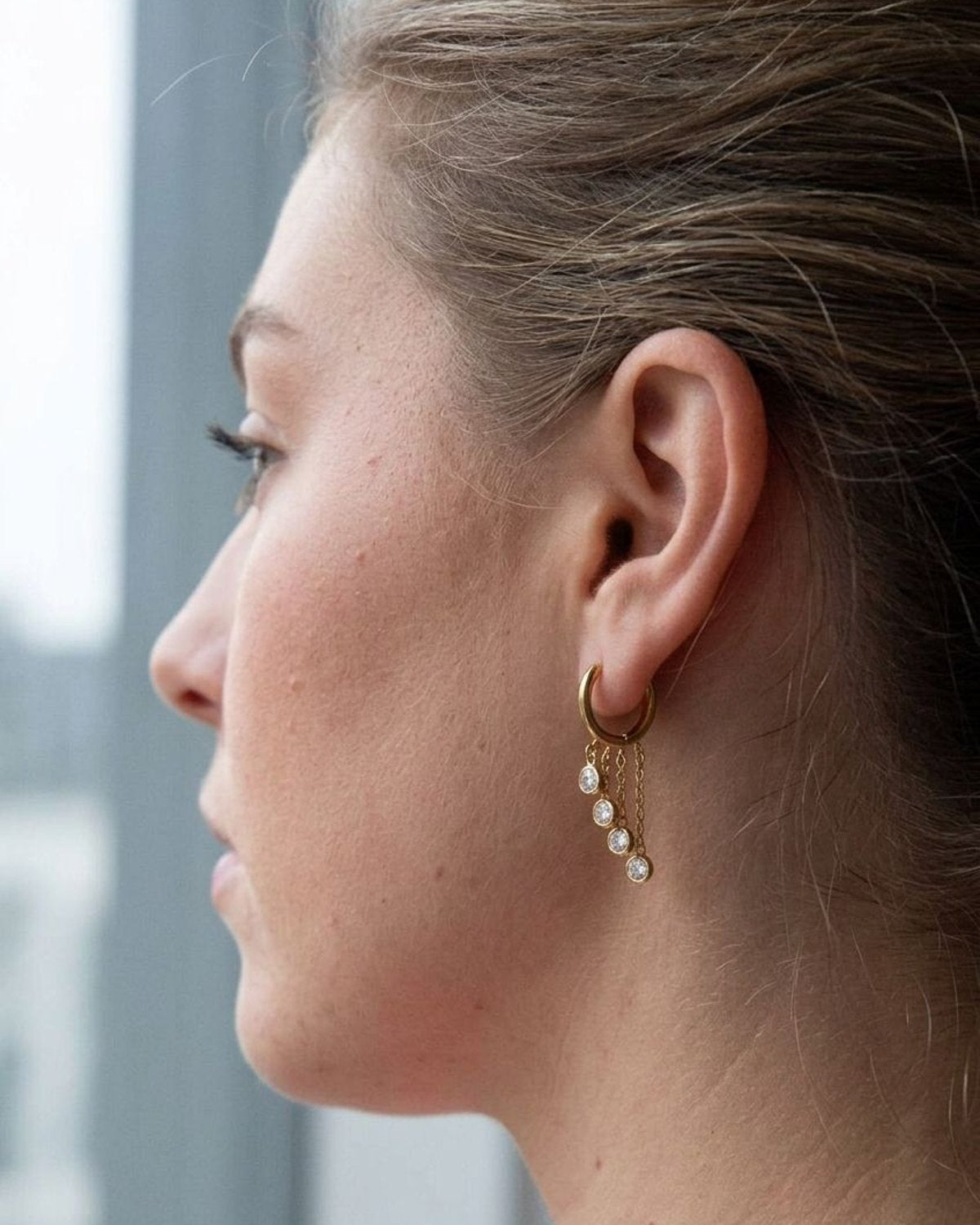 Profile view of a woman wearing a delicate stainless steel circle drop earring with zircon accents.