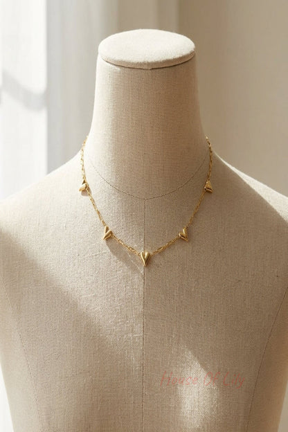 Close-up of a delicate gold-tone stainless steel heart link necklace on a neutral mannequin, highlighting craftsmanship and subtle sparkle in natural studio light.