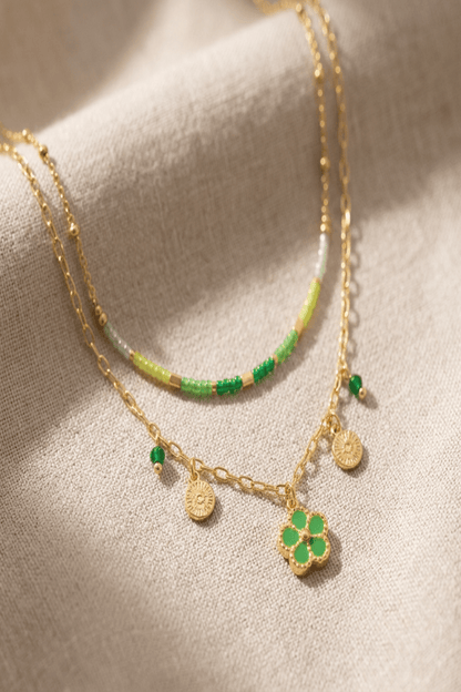 Close-up of the playful layered flower necklace highlighting intricate beadwork, tiny floral charm, and gold-tone chains on neutral fabric with natural light.