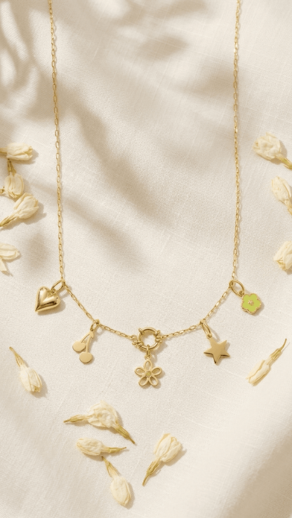 Gold chain necklace featuring heart, cherry, flower, and star charms, displayed on a textured white fabric with petals.