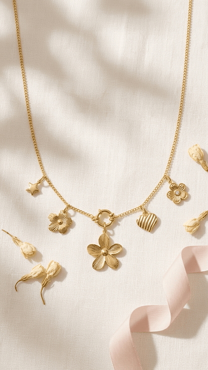 Gold-tone charm necklace featuring flower, heart, and star pendants on a delicate chain, set against soft fabric.