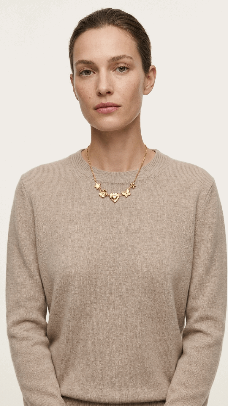 Gold chain necklace featuring charms of a star, flower, heart, and butterfly on a woman in a beige knit sweater.