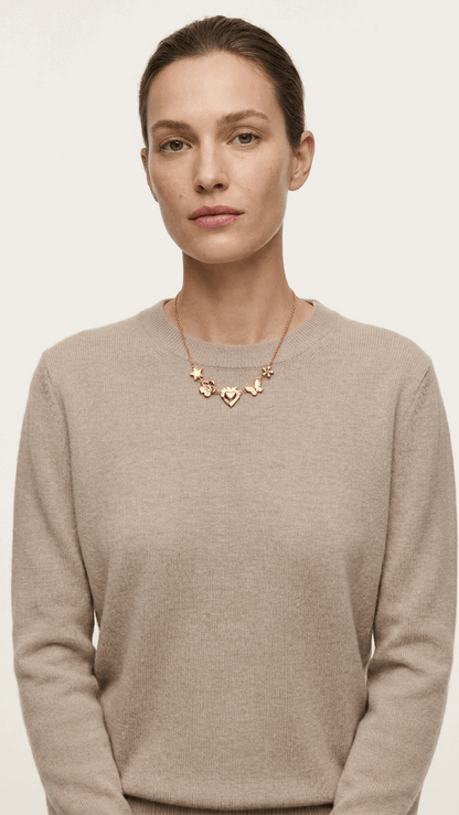 Gold chain necklace featuring charms of a star, flower, heart, and butterfly on a woman in a beige knit sweater.