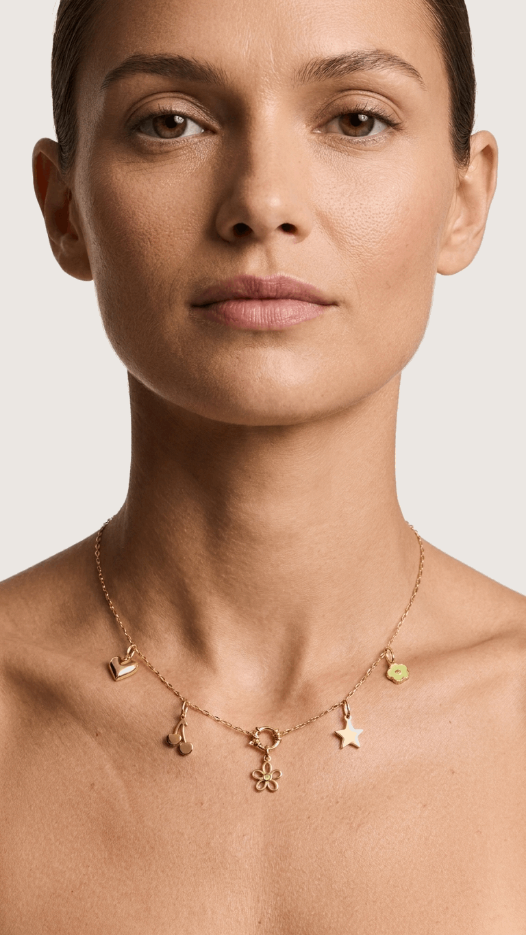 Delicate gold chain necklace featuring heart, cherry, star, and small flower charms on a woman's neck.