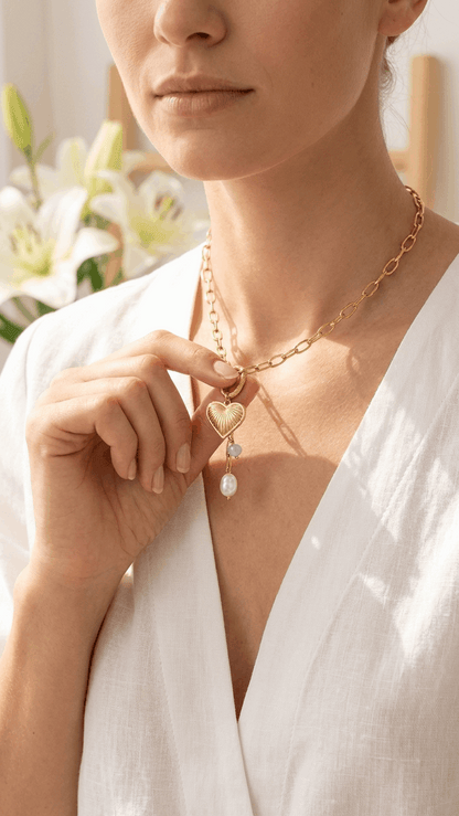 Gold chain necklace with a ribbed heart pendant, small blue bead, and a white pearl charm worn by a woman.