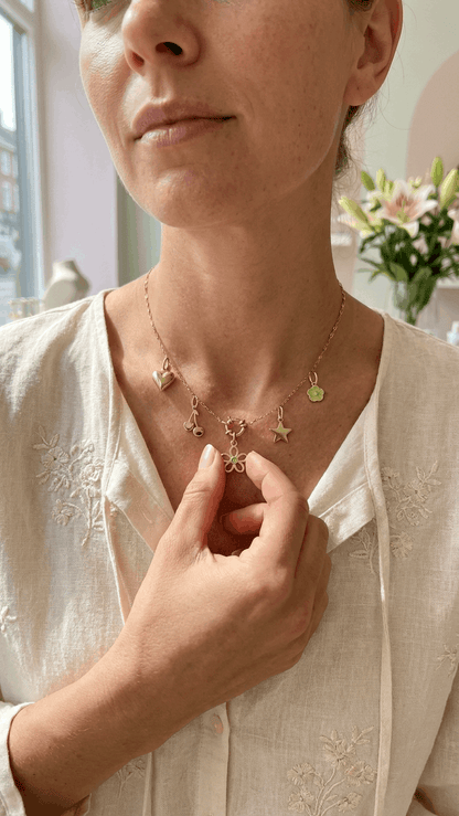 Gold chain necklace featuring dangling charms including a heart, cherry, star, flower, and small green petal flower.