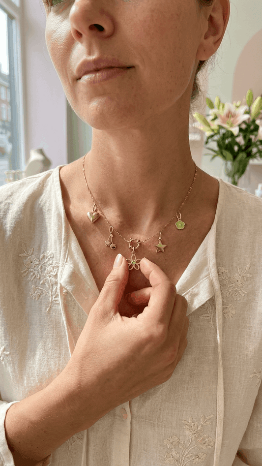 Gold chain necklace featuring dangling charms including a heart, cherry, star, flower, and small green petal flower.