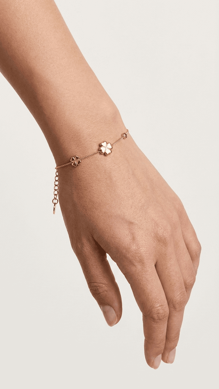 Gold Lucky Clover charm bracelet on a wrist, featuring two clover charms and a small pink stone accent.
