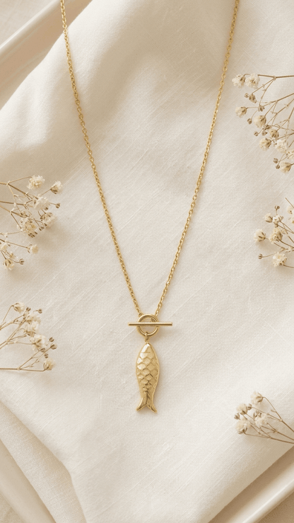 Gold Catching Vibes necklace with a detailed fish pendant on a delicate chain with a toggle clasp on a white cloth.