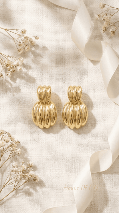 Chunky Vibe gold-plated ribbed dome hoop earrings on textured cream fabric with white silk ribbon and dried flowers.