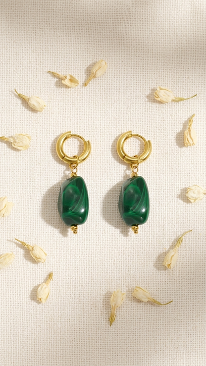 Gold hoop earrings featuring green, pebble-shaped stone charms by House of Lily, set against a floral background.