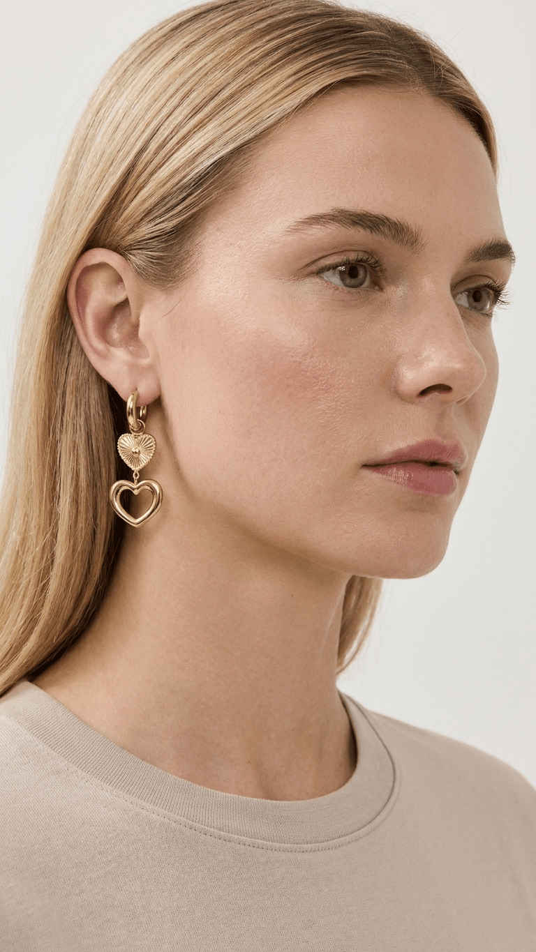 Model wearing Golden Heartcore Dangles: gold hoop earrings with small textured heart and open heart charms.
