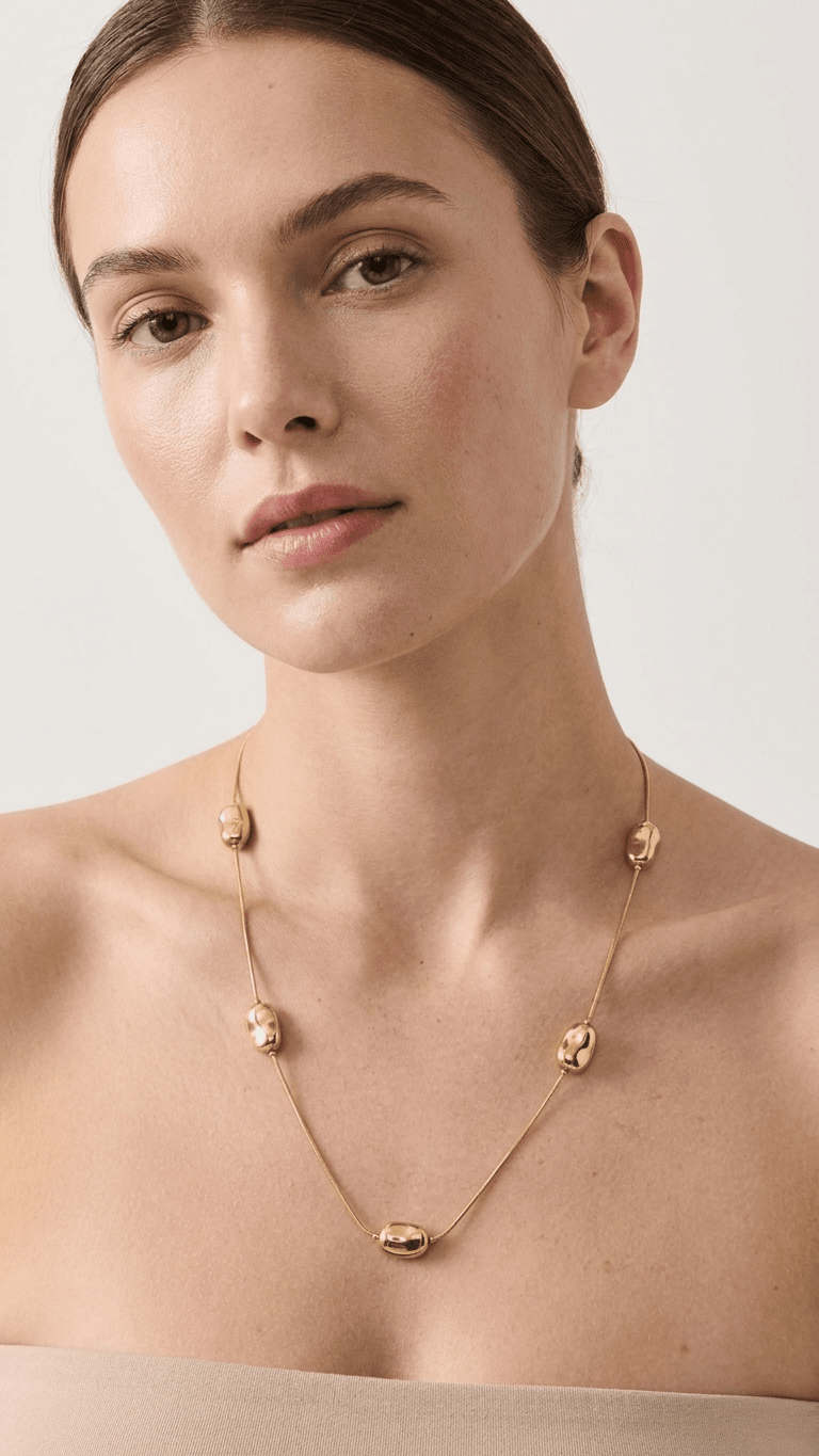 Modern gold chain necklace featuring five smooth, bean-shaped gold beads, worn by a woman against a neutral background.