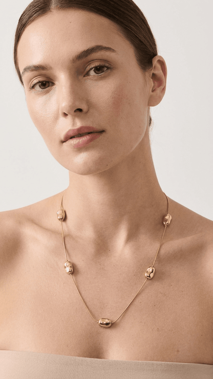 Modern gold chain necklace featuring five smooth, bean-shaped gold beads, worn by a woman against a neutral background.