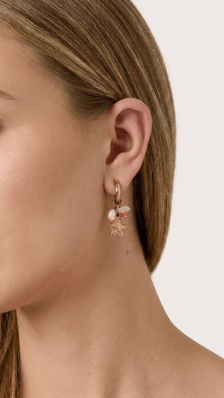A model wearing a gold Stardust click hoop earring featuring a small star charm, a white pearl, and tiny colorful beads.