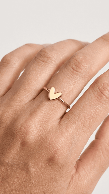 Minimalist gold band ring featuring a small, polished, solid heart-shaped charm on a slender finger.