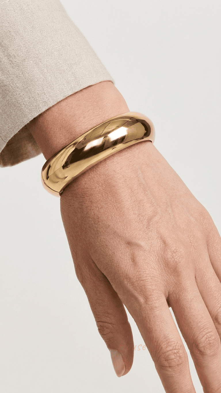 Chunky, polished gold hinged bangle bracelet worn on a wrist against a neutral background.