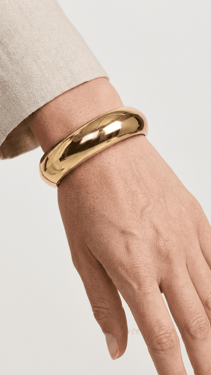 Chunky, polished gold hinged bangle bracelet worn on a wrist against a neutral background.