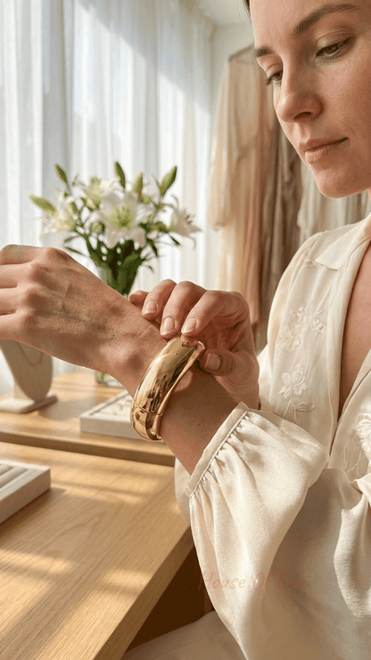 Woman wearing a polished, chunky gold hinged bangle on her wrist in a bright, airy jewelry store setting.