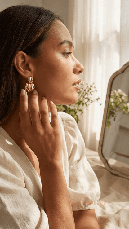 Chunky Vibe Hoops: small, ribbed gold-plated huggie earrings worn by a woman in a sunlit bedroom setting.