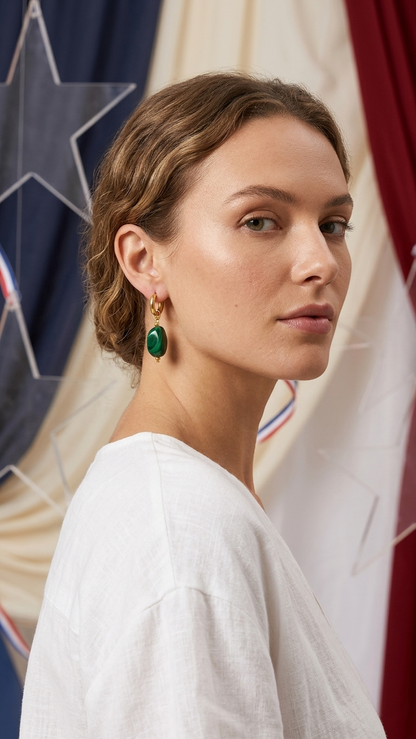A woman wearing House of Lily's Dreamy Jelly Pebble earrings: gold hoops with smooth, green malachite-style pendants.