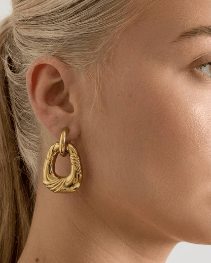 A person wearing a thick, textured gold hoop earring on their earlobe.
