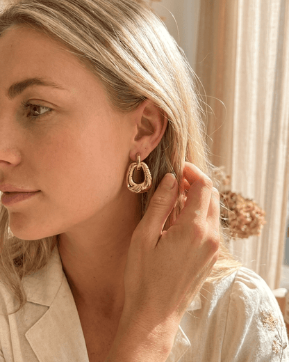 Close-up of a woman wearing chunky, gold-toned, twisted geometric dangle earrings.