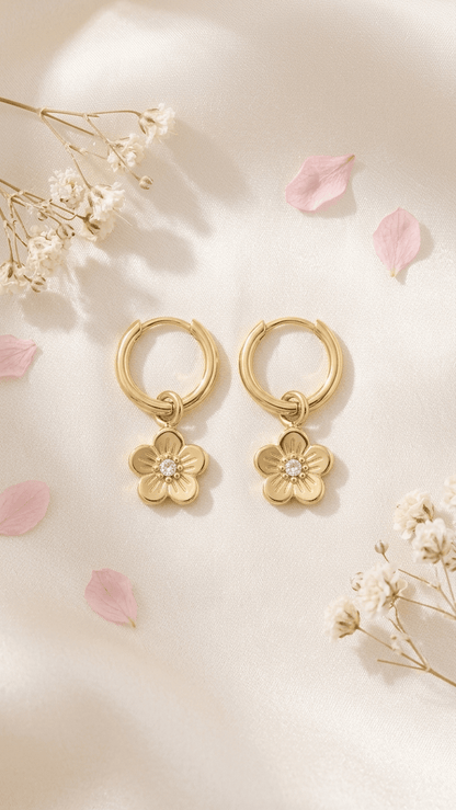 Gold hoop earrings with dainty flower pendants, featuring a central rhinestone on a light, floral-themed background.