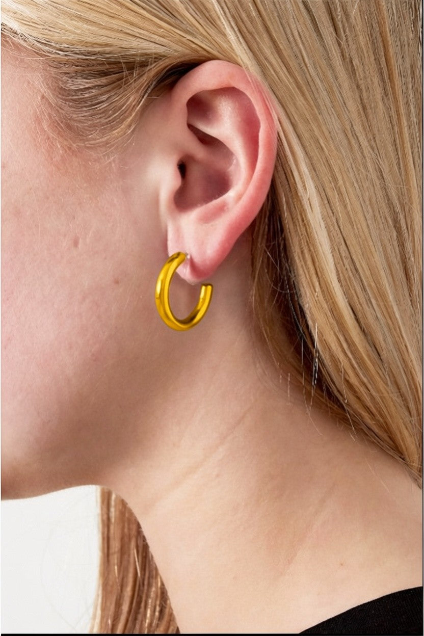 Thick gold hoop clip-on earring worn on a woman's earlobe; minimalist, polished round design.