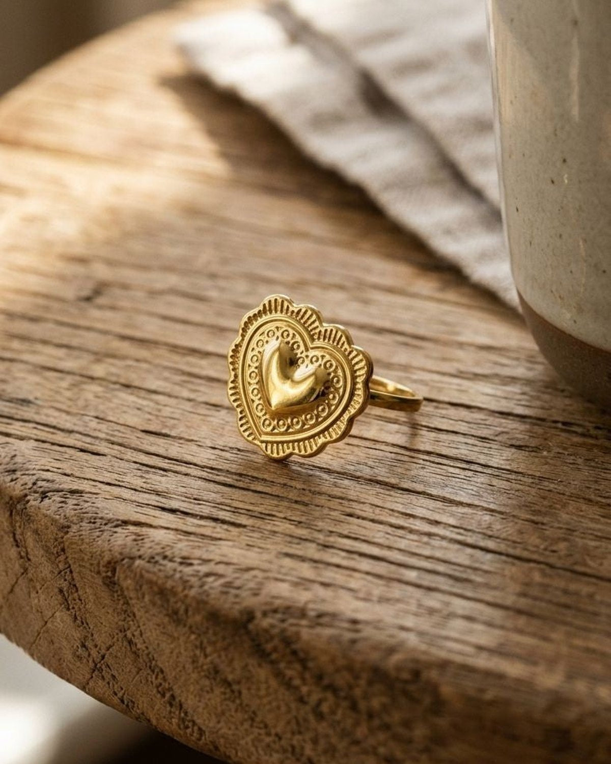 Small gold-tone hammered heart ring with scalloped edges on rustic wood, showcasing delicate craftsmanship and textured surface.