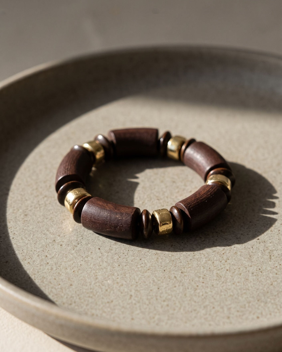 Retro wooden beaded bracelet featuring dark brown cylindrical beads and gold-tone accents resting on a neutral ceramic tray.