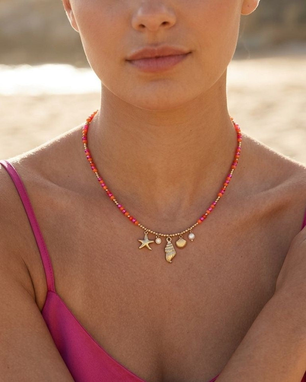 Close-up of seashell charm beaded necklace on feminine neckline, featuring glass beads, pearls, crystals, starfish and seashell charms, beach background