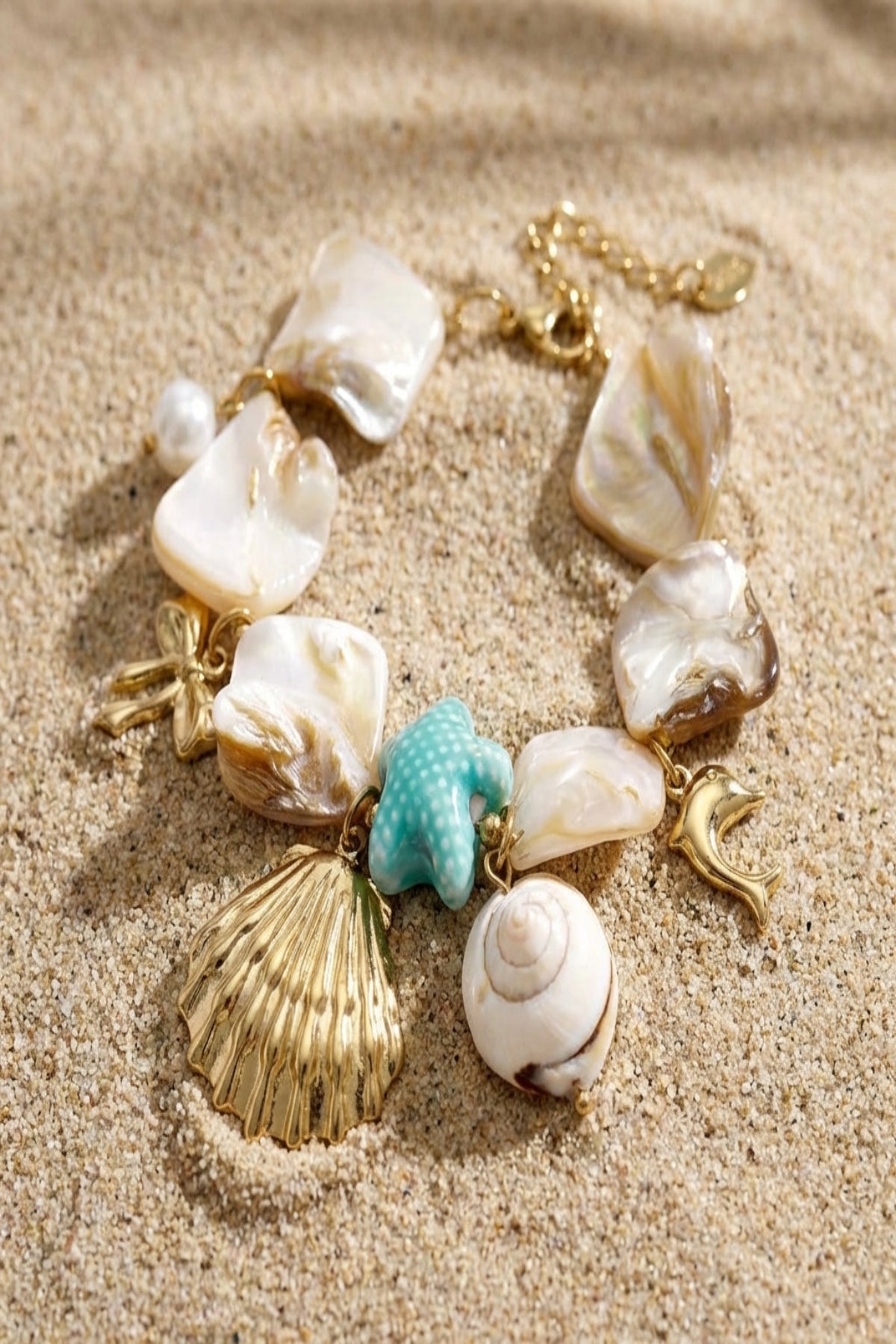 Close-up of seaside charm bracelet featuring natural shell pieces, beach charms like scallop shell, starfish, dolphin, on textured background.