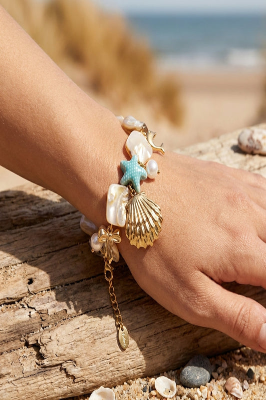 Woman wearing seaside charm bracelet with adjustable chain and playful charms, outdoor beach setting, natural daylight, summery vibe.