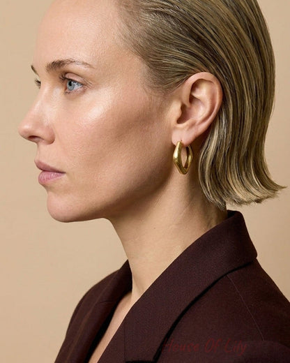 A profile view of a woman wearing thick gold-colored rectangular hoop earrings.