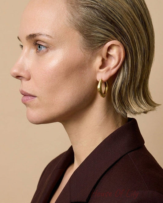 A profile view of a woman wearing thick gold-colored rectangular hoop earrings.