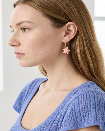 Gold hoop earring with a dangling textured pink starfish pendant, worn on a model.