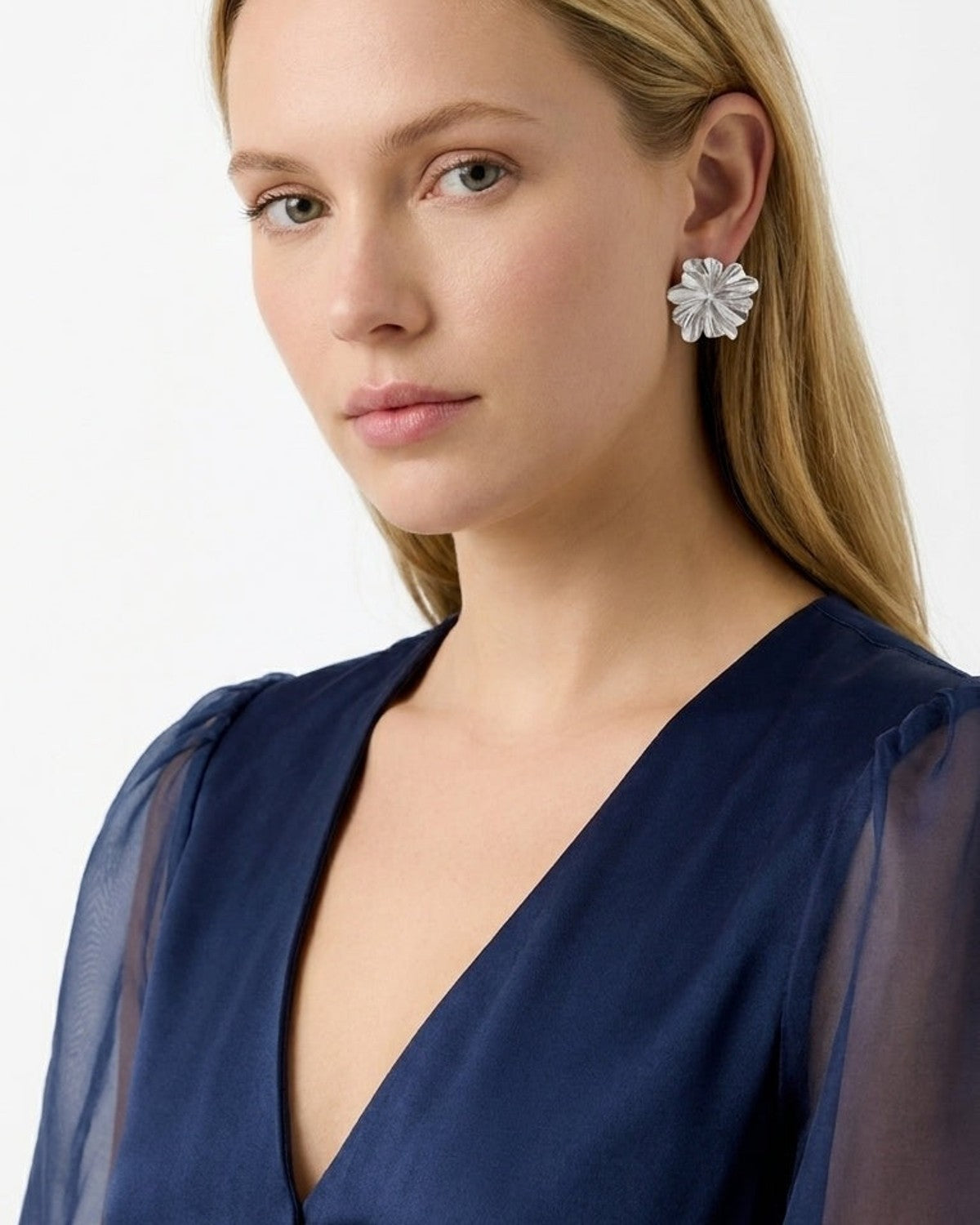 A model wearing shiny silver flower-shaped stud earrings and a navy blue top.