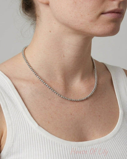 A person wearing a shiny silver beaded necklace with round 5mm beads around their neck.