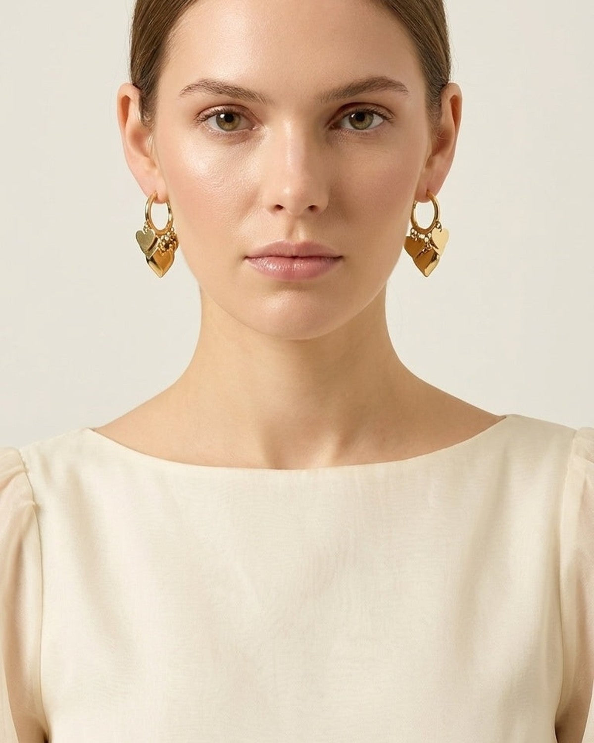 Gold hoop earrings with stacked heart charms worn by a model.