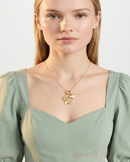 Woman wearing a gold pendant necklace with a flower and heart charm on a chain.