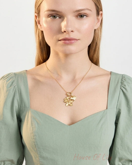 Woman wearing a gold pendant necklace with a flower and heart charm on a chain.