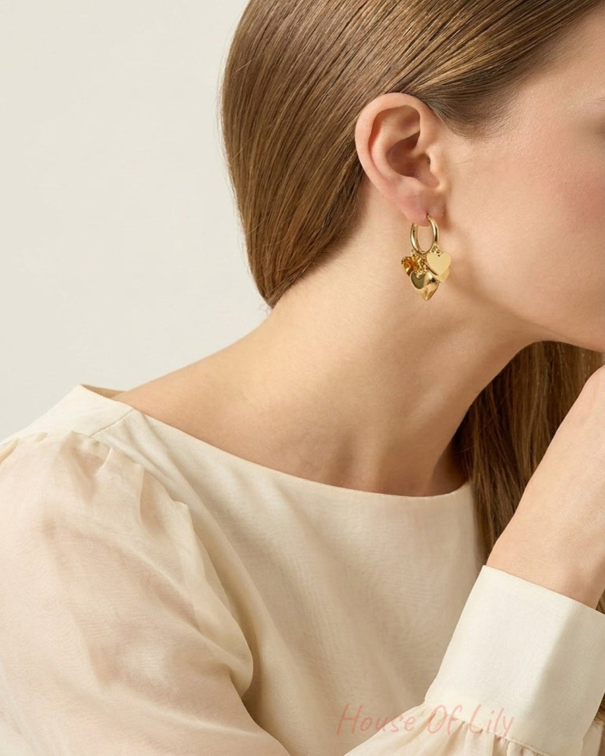 Gold hoop earrings with multiple dangling heart charms worn on a person's ear.